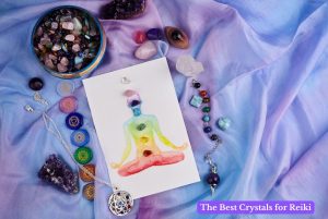 Flat lay of Reiki crystals including rose quartz, amethyst, clear quartz and tumbled chakra stones arranged around a watercolour chakra card on lilac silk